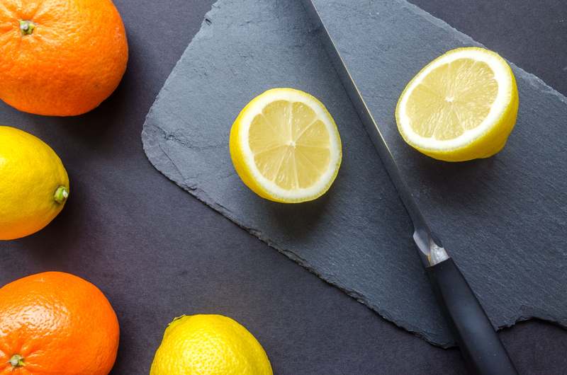 Side view of hands using a zester on a lemon with visible citrus oil spray and zest curling into a small bowl
